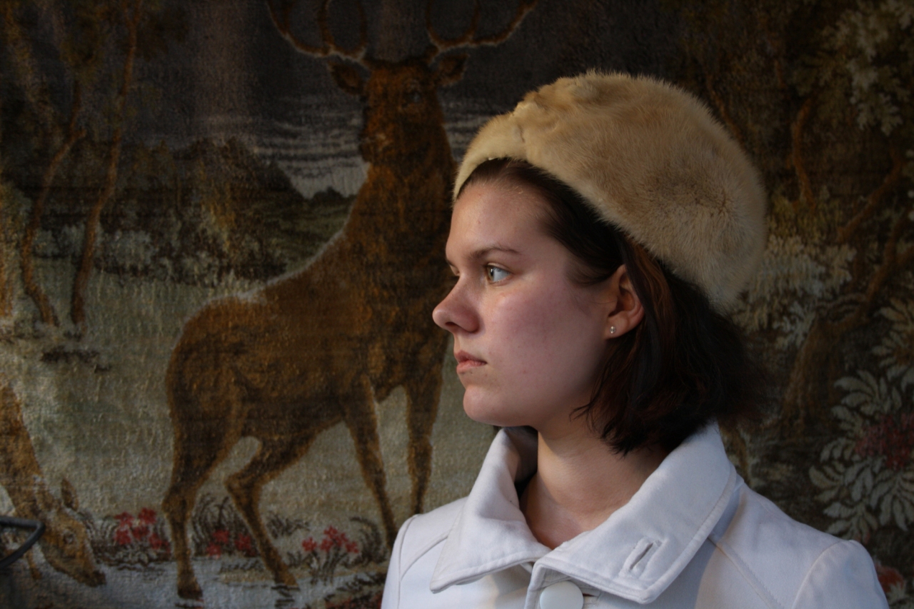 Photograph of a person dressed in a pale coat from the chest up with a fur hat.